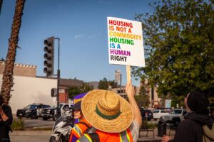 Protestor with a straw hat holding a sign in favor of tenant protections.